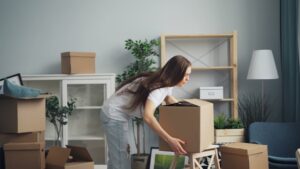Woman packing a cardboard box in a living room with several boxes and furniture around.